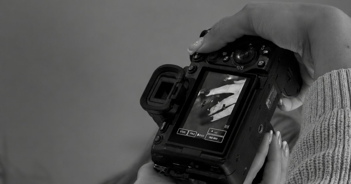 Black and white close-up of hands holding a mirrorless camera, the screen showing a shot of manicured hands during a Link Creative content shoot